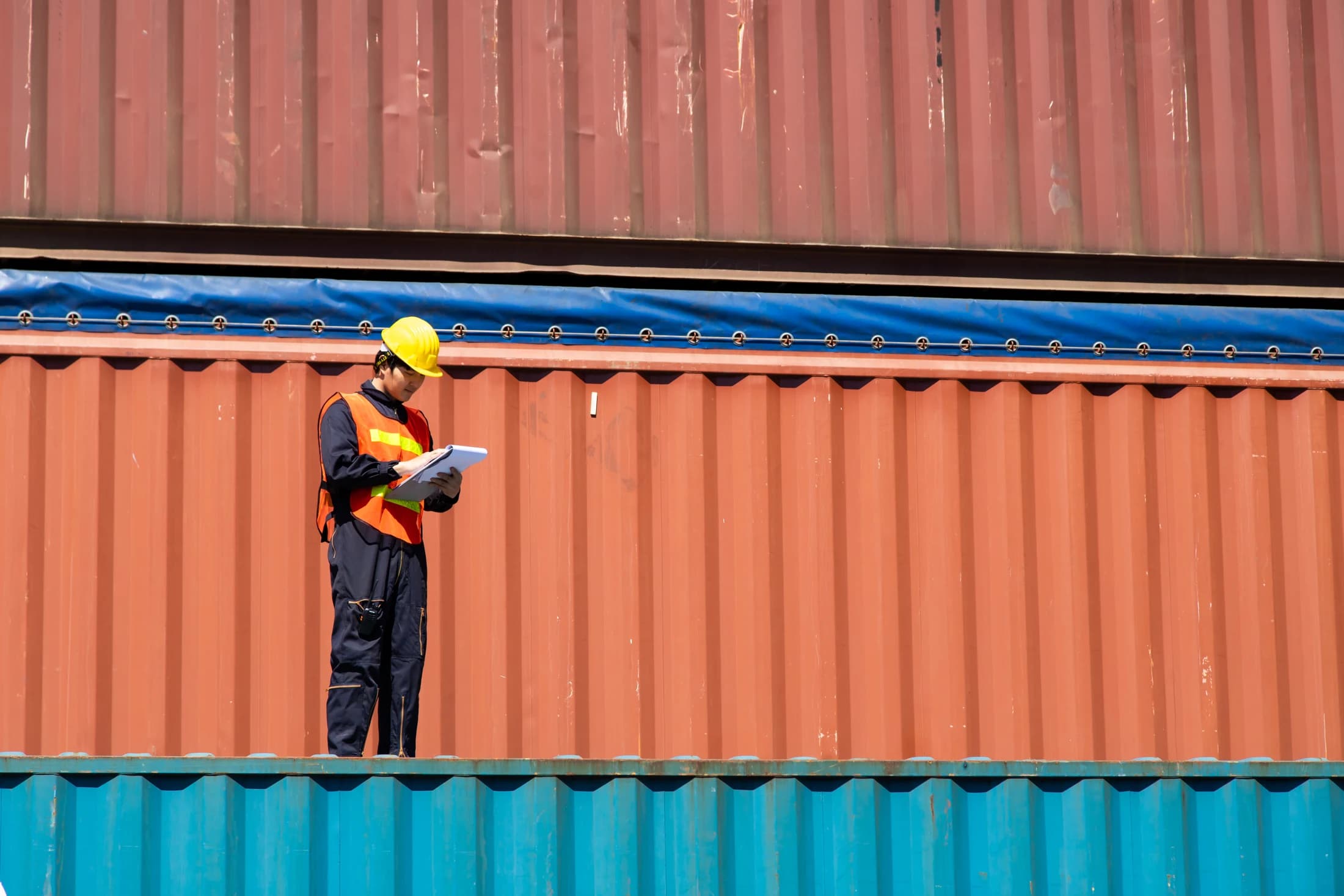 A worker reviewing documents beside shipping containers